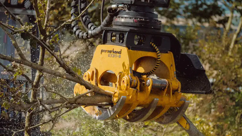 Yellow Powerhand EX36-B forestry grapple closing its tines on a branch, with debris thrown into the air around the head