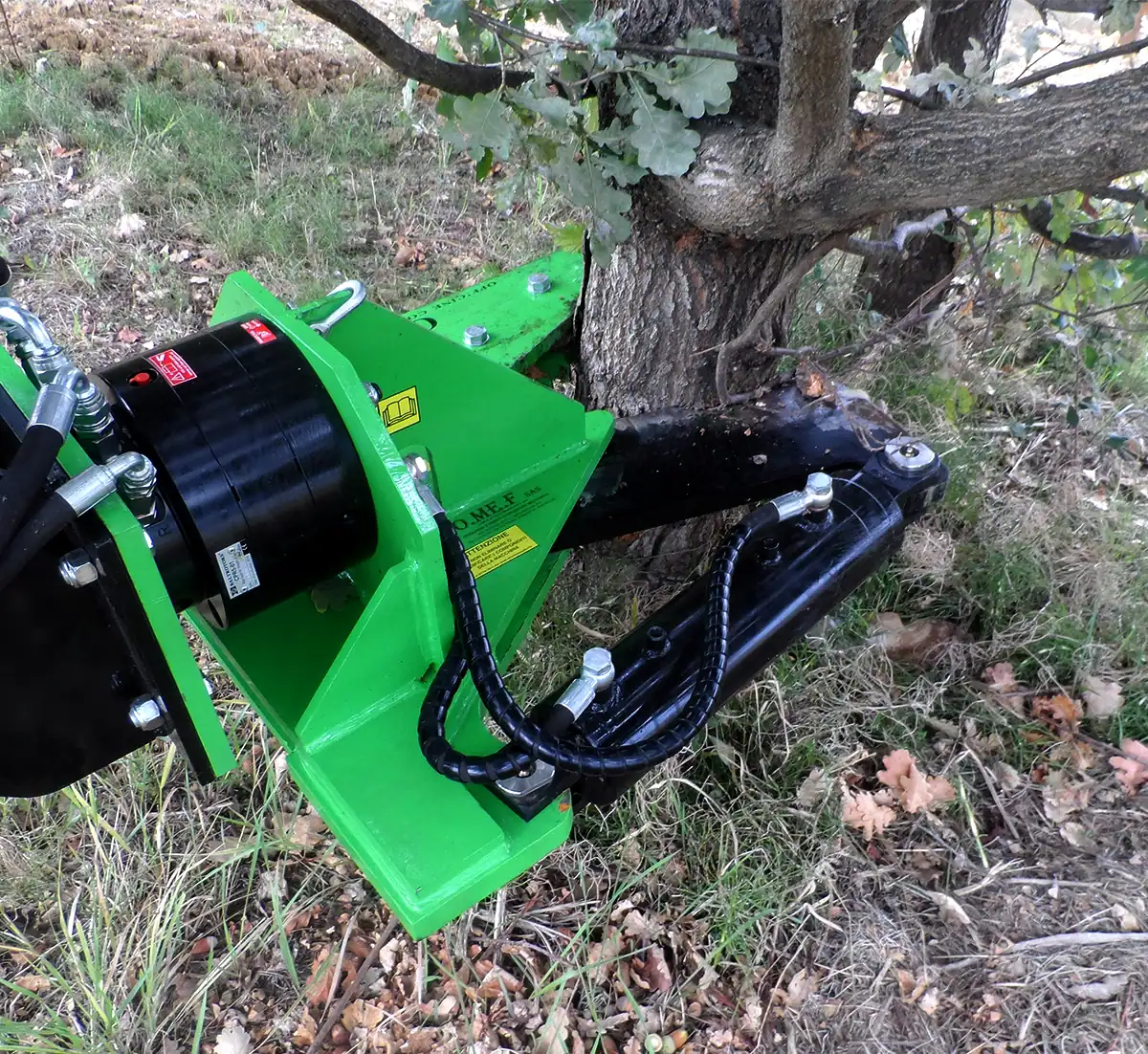 OMEF CS series forestry pruner with its cutting bar engaged at the base of an oak, hydraulic motor and hoses visible at the mount